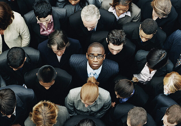 Businessman Looking up at Camera and Standing Outdoors Surrounded by a Large Group of Business People